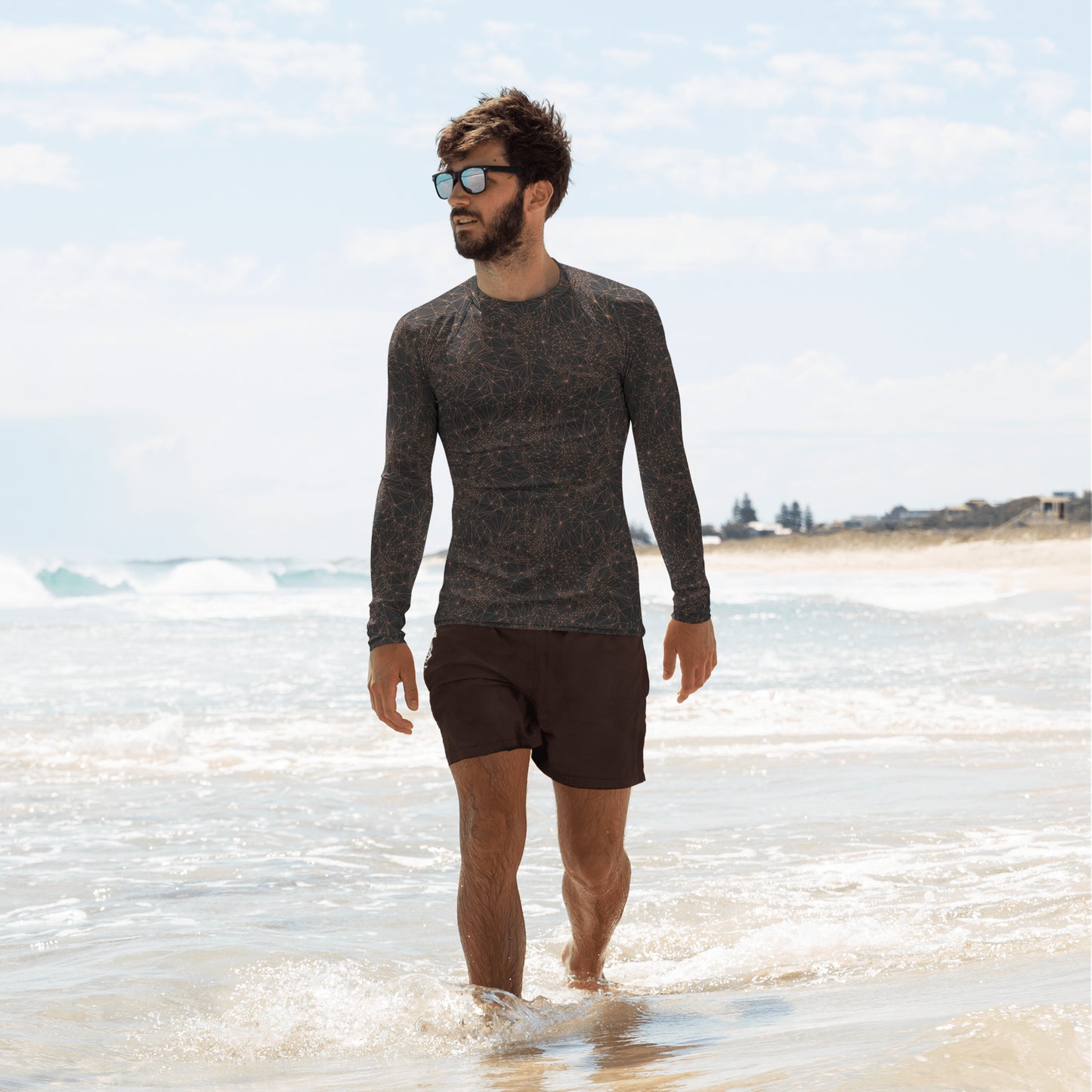 A man wearing Tri-Mesh Geometric Men's Long Sleeve UV 50+ Shirt Dark Gray and Orange while walking along a beach.